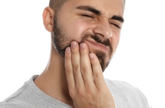 man with beard in need of emergency dentistry holding jaw in pain