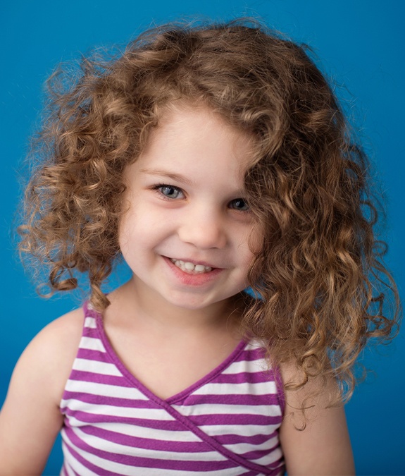 little girl with curly hair smiling after receiving dental sealants