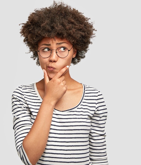 Woman in glasses and striped shirt thinking about dental crowns in Mansfield