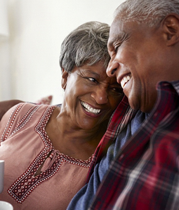 An older couple sitting on a couch and drinking tea while smiling and showing off their bridges in Mansfield