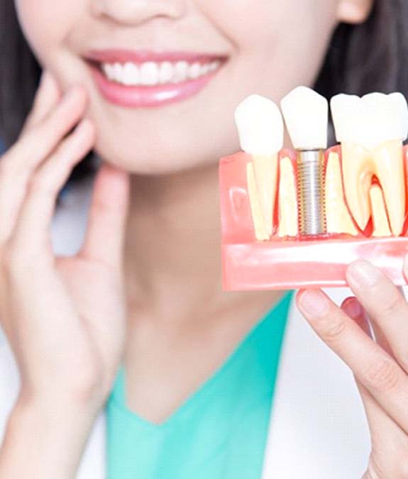 woman paying attention while dentist shows her a dental implant example