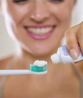 woman putting toothpaste onto an electric toothbrush