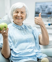 Senior female dental patient, holding apple and giving thumbs up
