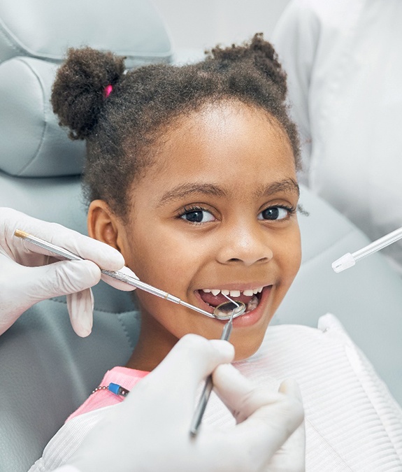 A young girl having her teeth checked and cleaned by a dentist and hygienist during a visit