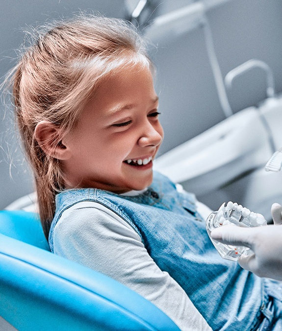 A little girl watching her dentist use a mouth mold and toothbrush to explain how to brush her teeth at home