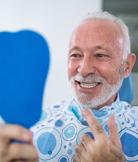 older man checking smile in blue mirror after dental bridge placement