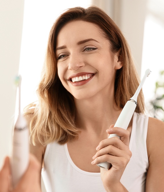 woman smiling at herself in mirror while holding toothbrush