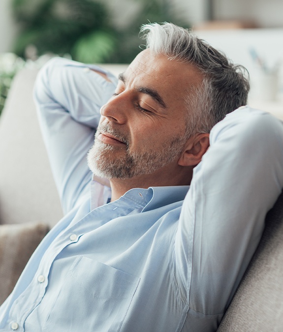 man leaning back and relaxing with hands behind head after sedation dentistry visit