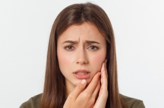 woman in need of restorative dentistry holding cheek with both hands