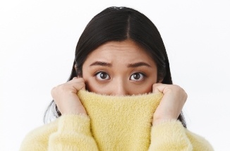 woman covering face with yellow sweater in need of sedation dentistry for anxiety