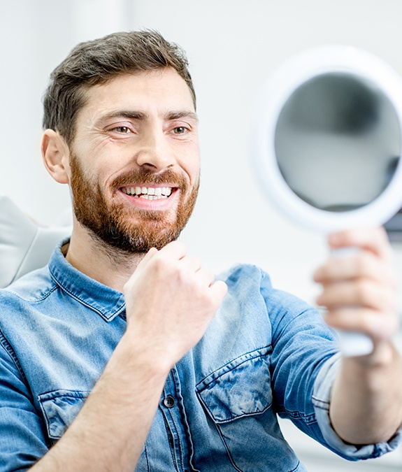 man with beard checking smile in circle mirror after porcelain veneer placement